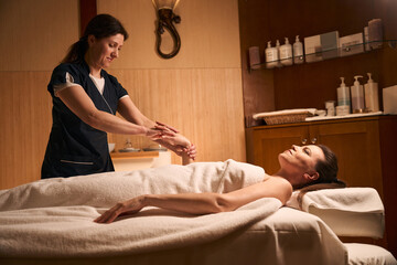 Skilled masseuse giving hand massage to calm spa client