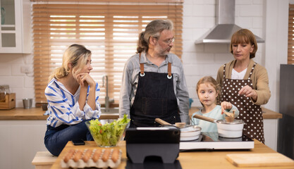Multi-generational family members explore new and tasteful recipes on a tablet, make healthy food choices, cook, and enjoy meals together. Family gatherings help renew and strengthen relationships.