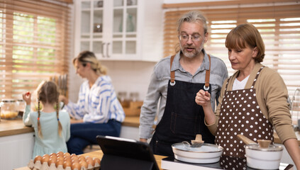 Multi-generational family members explore new and tasteful recipes on a tablet, make healthy food choices, cook, and enjoy meals together. Family gatherings help renew and strengthen relationships.