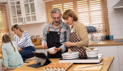 Multi-generational family members explore new and tasteful recipes on a tablet, make healthy food choices, cook, and enjoy meals together. Family gatherings help renew and strengthen relationships.