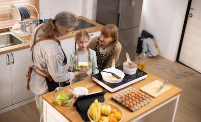 Multi-generational family members explore new and tasteful recipes on a tablet, make healthy food choices, cook, and enjoy meals together. Family gatherings help renew and strengthen relationships.