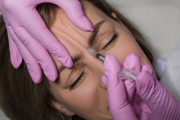 Close up of beautician expert's hands injecting botox in female forehead.