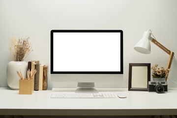 Front view of blank screen computer with keyboard, lamp, picture frame and books on white table