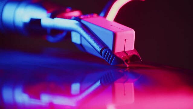 Needle of the headshell of the turntable slides on the surface of the record close up until the record ends and it stops close up during the studio recording of the vinyl session in a color light
