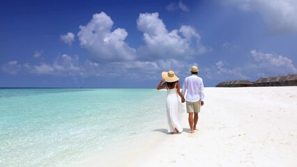 A elegant couple on holidays walks down a tropical paradise beach with fine sand anf turquoise sea - Powered by Adobe