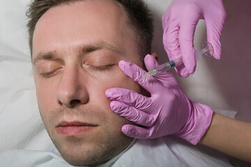 Handsome man gets beauty facial injections. Photo of an Attractive man gets Botox injection in eyes zone. Aesthetic Cosmetology concept