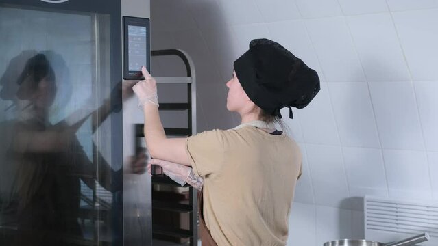 the baker girl touches the oven control panel with her finger.