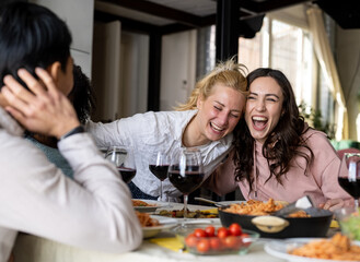 Group of best friends sitting at table on a holiday and holiday day, Italian food spaghetti and red wine, two girls hug and laugh happy