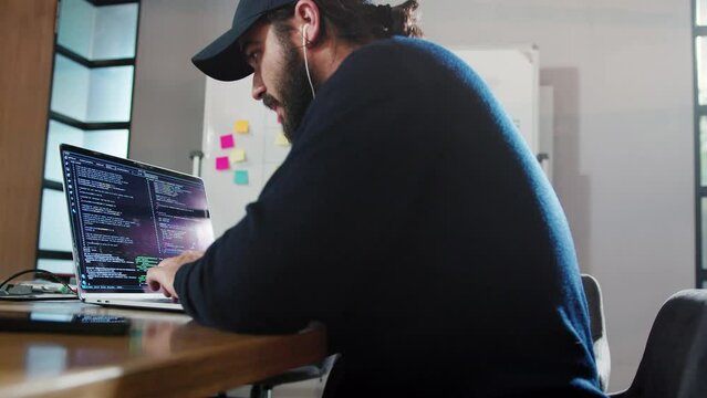 Computer programmer writing a code in an office. Male software developer sitting and working on a laptop. Creative business man working in a tech company.