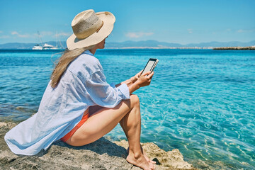 Happy woman outdoors lifestyle watching, reading on tablet ebook on the beach in summer day....