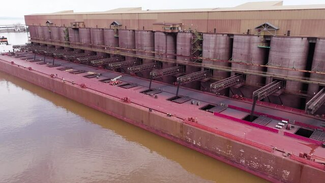 Iron ore dock with conveyor belts loading taconite natural resource minerals into large freight vessel with workers