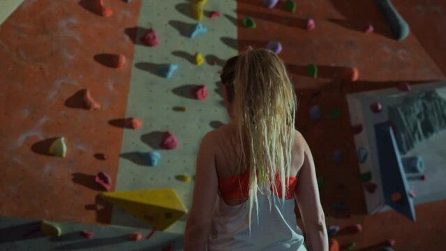 A young, purposeful, athletic blonde millennial woman goes forward to the climbing wall with the mood to win and starts climbing up the wall. The beginning of a difficult path. High quality 4k footage