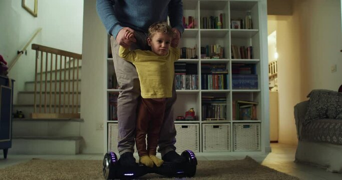 Portrait of Little Kid Enjoying Riding a Hoverboard with his Father in Living Room at Home. Man Introducing his Toddler Son to Technological Gadgets. Family Time and Bonding Concept