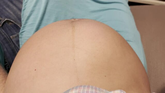 mom-to-be resting on couch, with exposed pregnant belly and baby kicking and moving, wearing a teal long skirt