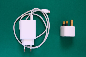 Mobile phone charger (USB type C) and UK adapter and on a dark green background, top view.