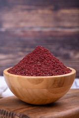 Sumac on wooden background. Dried ground red Sumac powder spices in wooden bowl. Close up