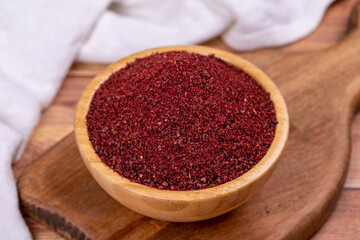 Sumac on wooden background. Dried ground red Sumac powder spices in wooden bowl