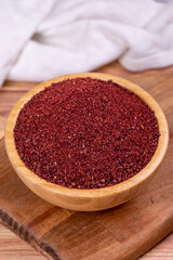 Sumac on wooden background. Dried ground red Sumac powder spices in wooden bowl. Close up