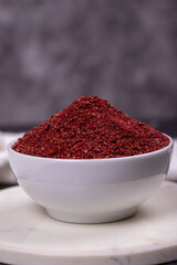 Sumac on dark background. Dried ground red Sumac powder spices in wooden bowl. Close up