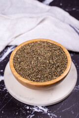 Dried crushed basil on dark background. Dried ground basil powder spices in wooden bowl. Spice concept. Close up