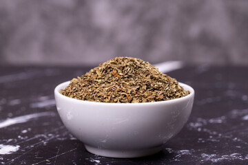 Dried crushed basil on dark background. Dried ground basil powder spices in ceramic bowl. Spice concept