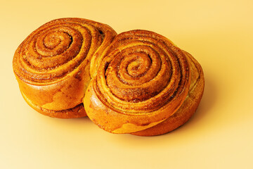 Two cinnamon buns covered with sugar on an orange background