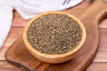 Dried crushed basil on wooden background. Dried ground basil powder spices in wooden bowl. Spice concept. Close up