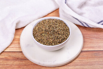 Dried crushed basil on wooden background. Dried ground basil powder spices in ceramic bowl. Spice concept