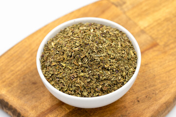 Dried crushed basil isolated on white background. Dried ground basil powder spices in ceramic bowl. Spice concept. Close up