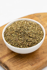 Dried crushed basil isolated on white background. Dried ground basil powder spices in ceramic bowl. Spice concept. Close up