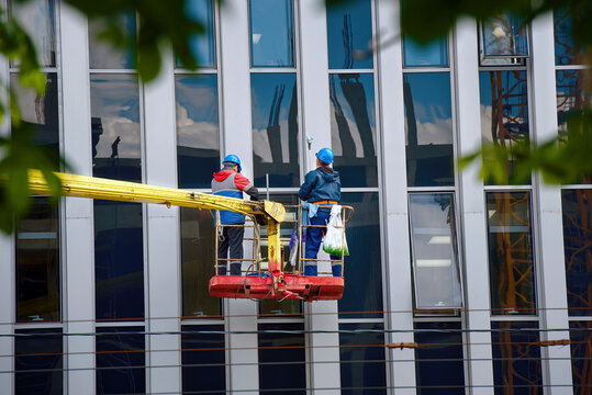 Window washing of high-rise office building in crane bucket. Workers team washing glasses windows at height in lifting platform. Window cleaner, building exterior wet wash. Clean service team