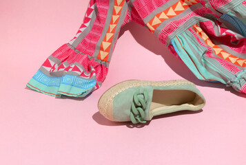 Minimal layout of women's pastel green shoe and a patterned summer dress. Sustainable fashion scene  on pink background.