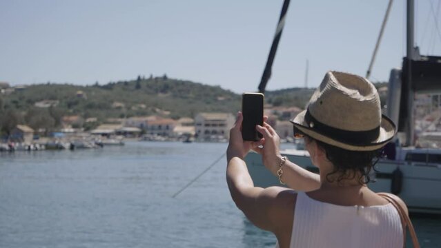 Woman taking pictures with smartphone of picturesque fishing village Gaios with port in Paxos with turquoise sea, Ionian islands of Greece, slow motion