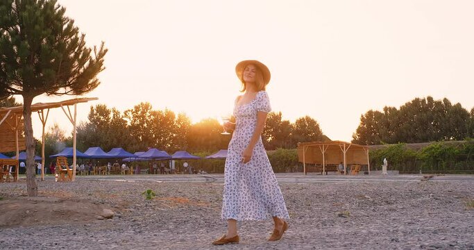Dreaming young woman enjoying summer with a glass of wine in hand on lovely sunny day. Smling woman walking near vineyards. Relax outdoor vacation lifestyle concept