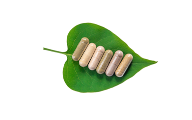 Herb supplement capsules on green leaf isolate on white background. Selective focus.