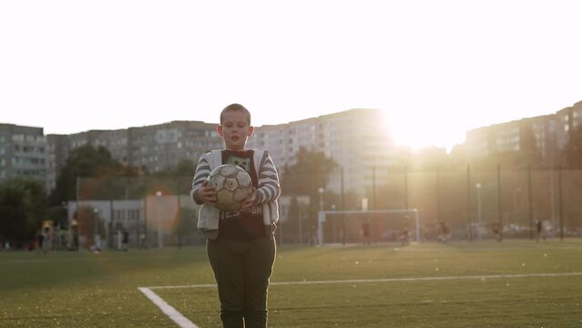 Caucasian boy 9 years old throws up and catchesold soccer ball with his hands, slow motion. Overweight child plays on sunny soccer field in residential area. Concept of active outdoor lifestyle.