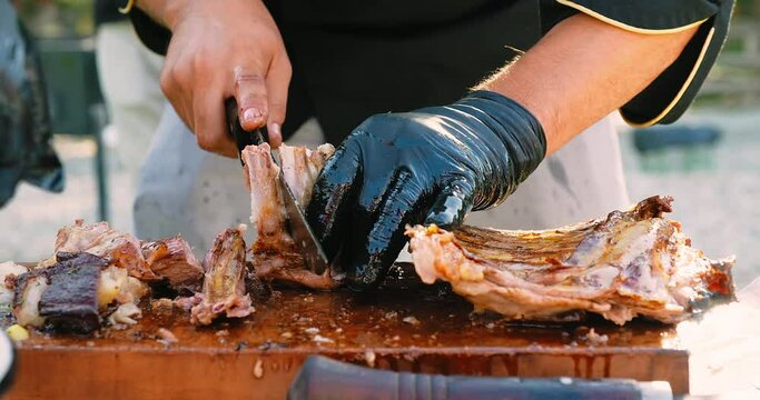 Summer barbecue party. Close-up of a chef's hands cutting slicing meat. Picnic meal. BBQ meat grill on fire for party