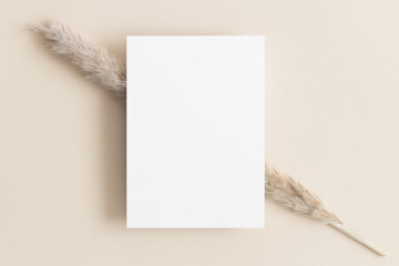 White invitation card mockup with a pampas on the beige table. 5x7 ratio, similar to A6, A5.