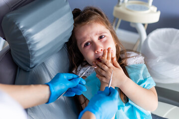 little brunette girl at the reception is crying, afraid. Pediatric dentistry