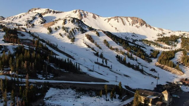 Aerial Cinematic drone early sunrise Spring Mammoth Mountain California ski trails and ski lodge parking lot gondola and chair lift to the left and up movement towards halfpipe