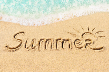 Summer word written on sand with blue sea wave on background. summer holidays and beach vacation concept