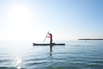 Fototapeta premium Side view of young woman floating on surf with paddle