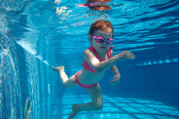 Portrait of cute little baby girl, toddler in pink swimsuit and goggles diving, swimming underwater...