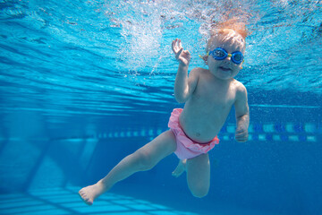 Cute, smiling, happy little baby girl, toddler in swimsuit and goggles swimming underwater in swimming pool. Enjoyment. Concept of sport, healthy and active lifestyle, childhood, fun and training