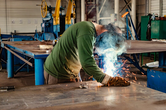 Industrial Welder With Torch and Protective Helmet in big hall welding metal profiles.