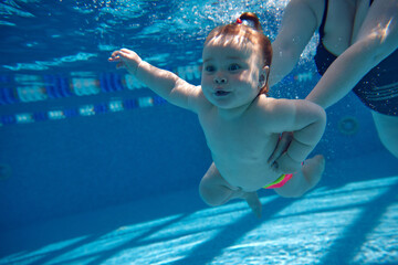 Cute, beautiful, little baby girl, toddler swimming underwater in swimming pool with instructor...