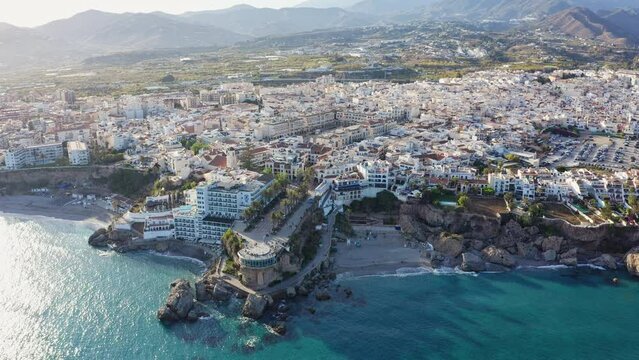 Aerial drone shot revealing the Andalusian coastal town Nerja, Balcon de Europa viewpoint in foreground and mountains in background