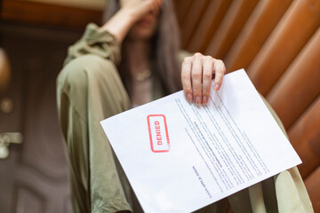 Young brunette long hair girl cries hysterically after being denied a mortgage loan. Depressive sad eviction female millenial holding rejection document copy space banner - obrazy, fototapety, plakaty