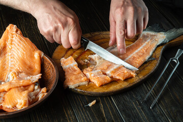 Close-up of a chef's hands with knives while cutting fresh fish on a cutting kitchen board before...
