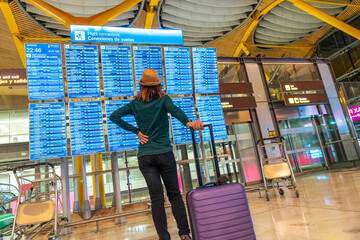 Obraz premium Tourist woman with suitcase at the airport looking at the information on screens in the terminal